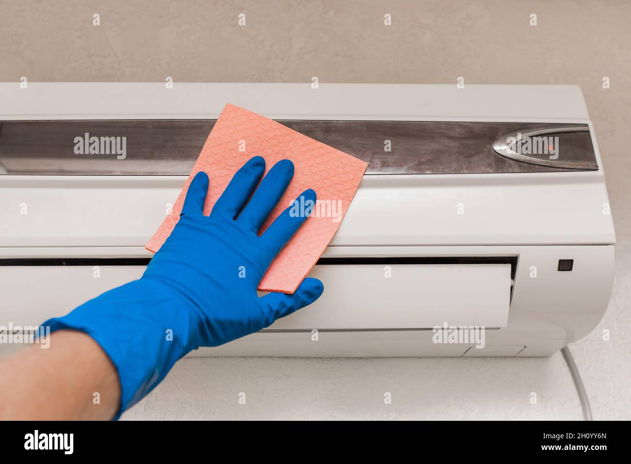 The hand of a man in a blue rubber household glove wipes and cleans the air conditioner. Maintenance and cleaning indoor service. Stock Photo