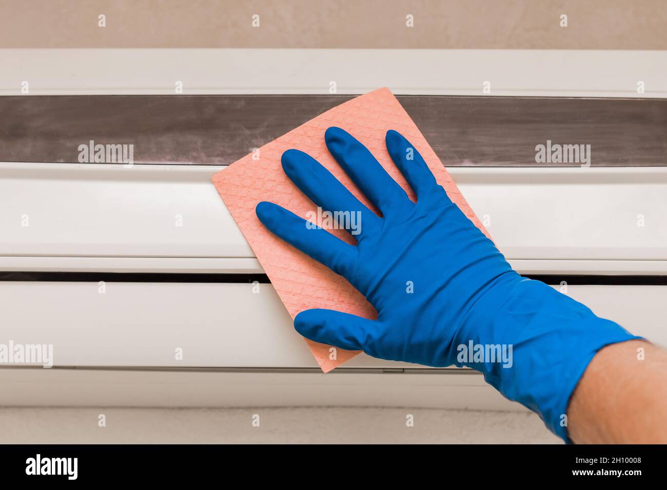 The hand of a man in a blue rubber household glove wipes and cleans the air conditioner. Maintenance and cleaning indoor service. Stock Photo