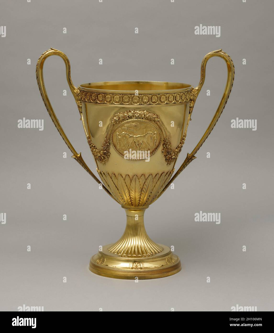 Trophy Cup, 1792–93. Peter Bateman (British, 1740-1825), Anne Bateman (British, 1748-1813). Silver gilt; overall: 59.7 x 40 cm (23 1/2 x 15 3/4 in.).  Silver fulfilled a prominent role in projecting wealth, status, power, and ritual in British life during the 1600s and 1700s. Elaborate forms such as this trophy, with its swags of flowers, neoclassical rosettes, and acanthus spears, not only represented wealth in its sheer silver weight but also provided royal and aristocratic owners a surface for displaying engraved coats of arms. Engraved on one side of this trophy cup can be found the arms o Stock Photo
