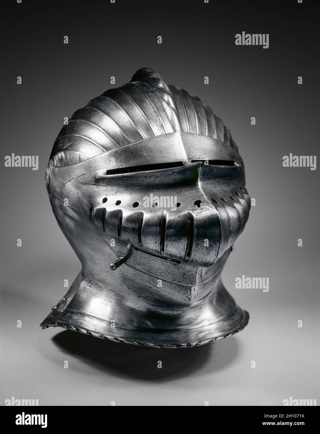 Close Helmet in Maximilian Style, c. 1510–30. Germany, Nuremberg(?), 16th century. Steel, brass rivets; overall: 29.2 x 34.9 x 23.5 cm (11 1/2 x 13 3/4 x 9 1/4 in.).  Distinguished by its regularly fluted surfaces, armor in this style was popularized in South Germany during the early 1500s. The style is usually called 'Maximilian,' as it was introduced during the reign of Emperor Maximilian I (1493-1519). The style reflects male costume of the period and the shift to the new rounded forms of the Renaissance. Other examples of this armor style may be seen nearby. Stock Photo