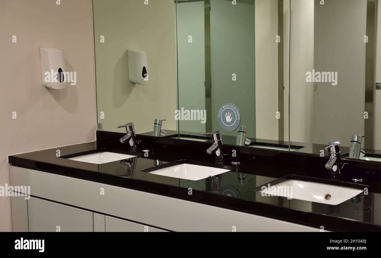 Row of 3 wash hand basins inset in black worktop with mirrors behind Stock Photo