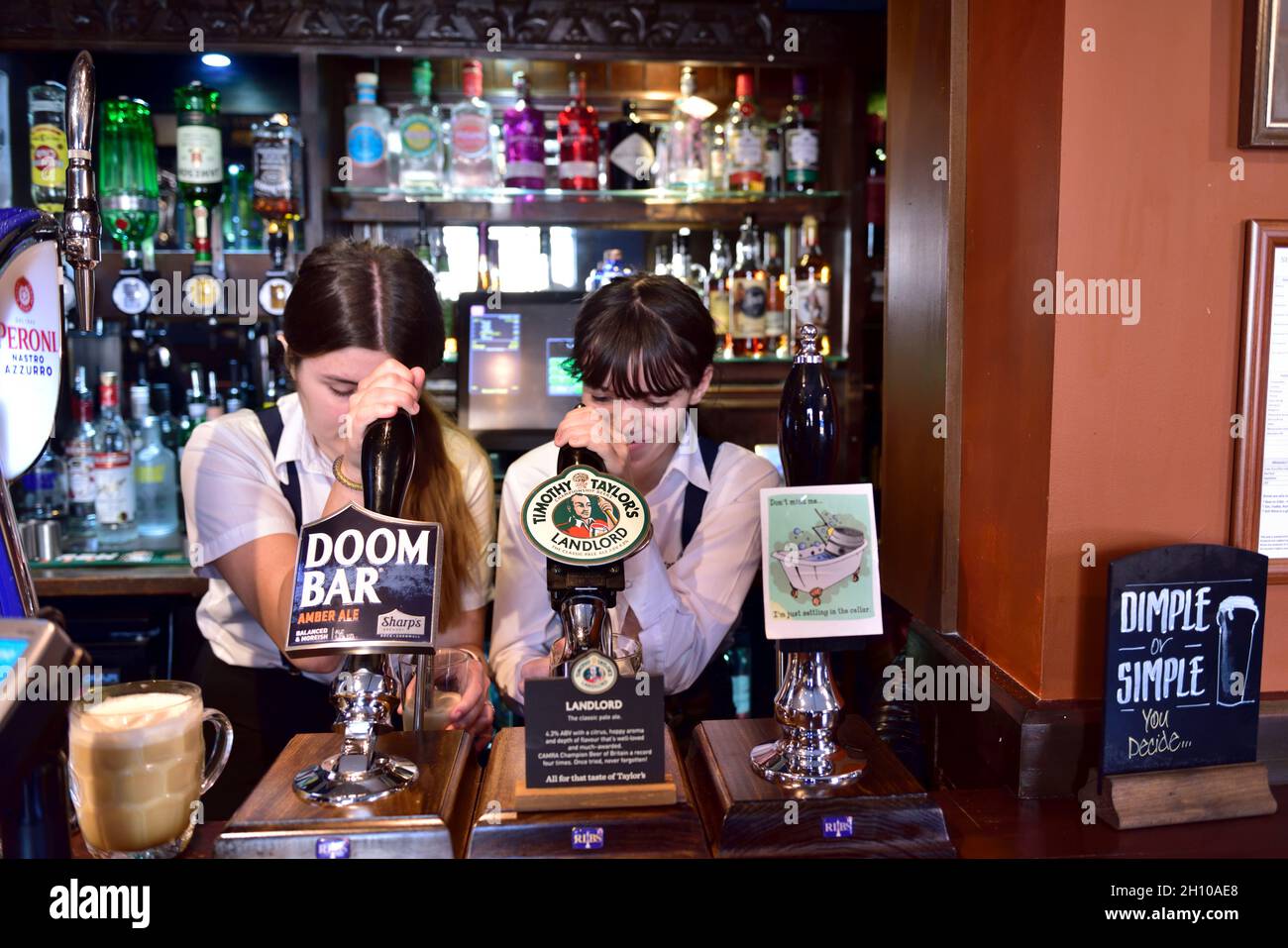 Two attractive female bartenders pulling pints behind hand beer pumps in Tap & Spile Birmingham pub, UK Stock Photo