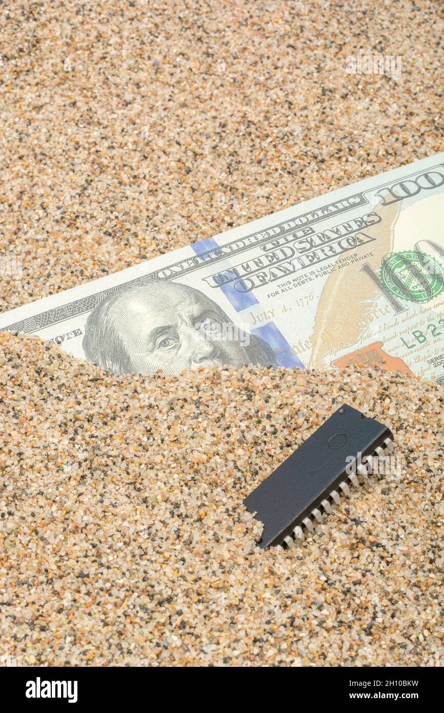 US $100 dollar bill / Benjamin Franklin banknote buried in sand with microchip. For US semiconductor chip shortages in the technology sector. Stock Photo