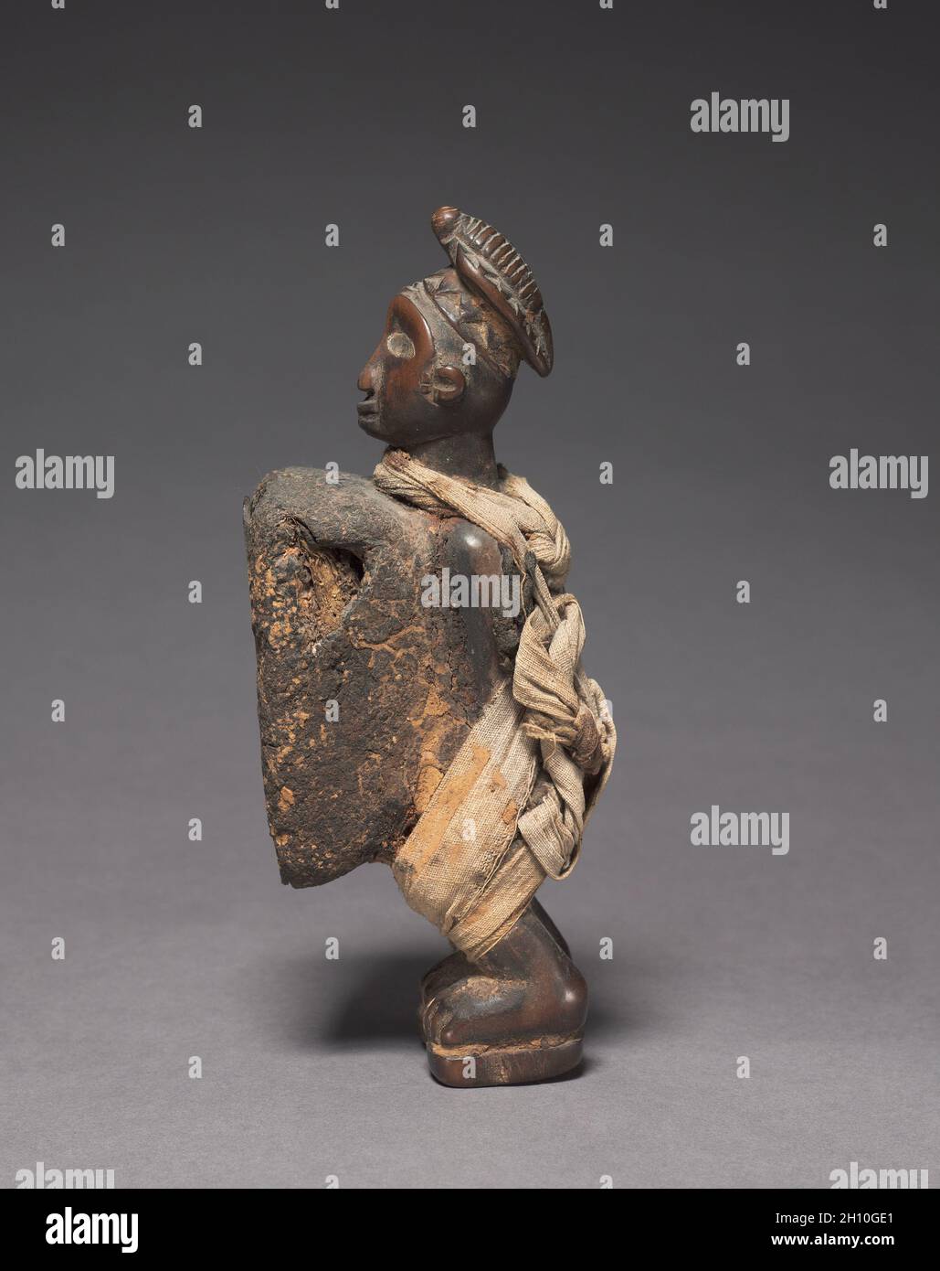 Male Figure (nkisi), late 1800s-early 1900s. Africa, Central Africa, Democratic Republic of Congo (most likely), Cabinda, or Republic of the Congo, probably Yombe-style maker. Wood, organic material (including resin), metalized glass, and cloth; overall: 17 x 5.3 x 7 cm (6 11/16 x 2 1/16 x 2 3/4 in.). Stock Photo