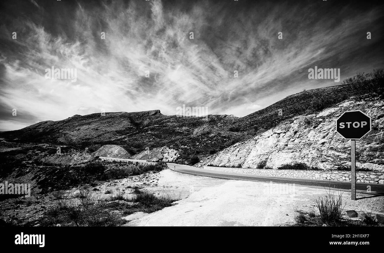 Grayscale shot of a stop sign on the road in the mountains Stock Photo