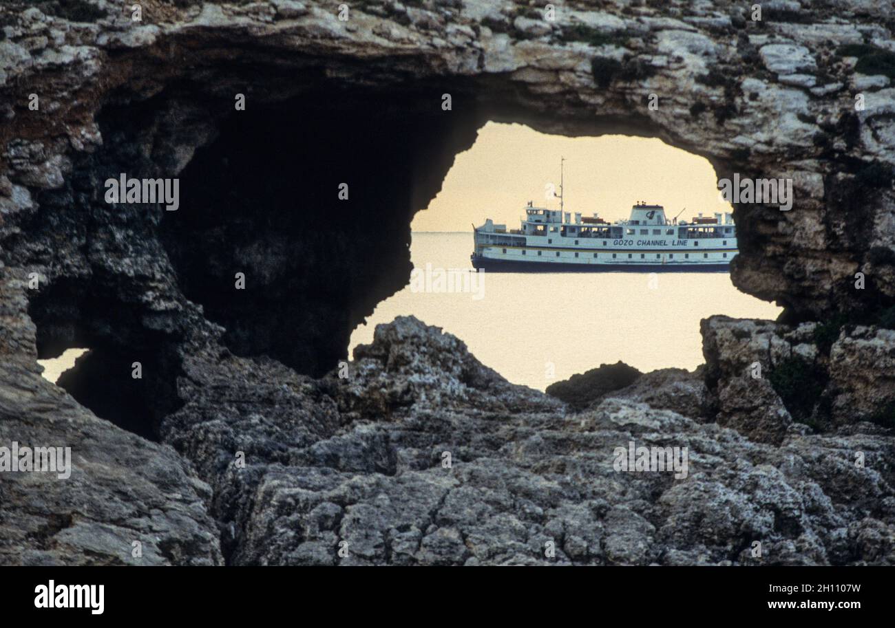 Fähre in der Meerenge zwischen Malta und Gozo gesehen durch einen Felsdurchbruch vor Comino - Ferry in the Gozo Channel seen through a hole in a rock off Comino island. Stock Photo