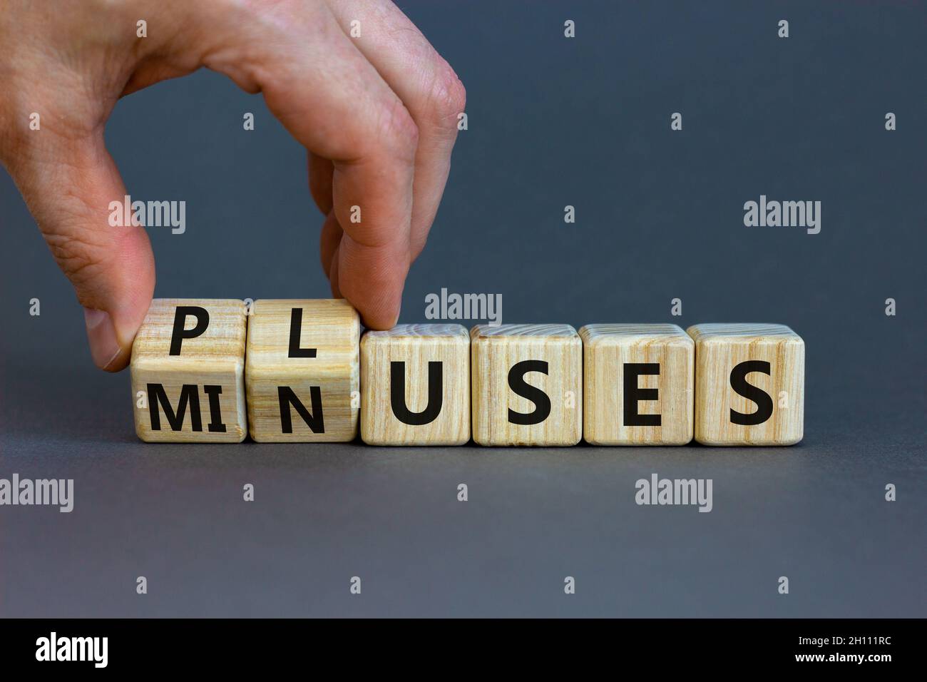 Pluses and minuses symbol. Businessman turns wooden cubes and changes the word 'minuses' to 'pluses'. Beautiful grey table, grey background. Business, Stock Photo