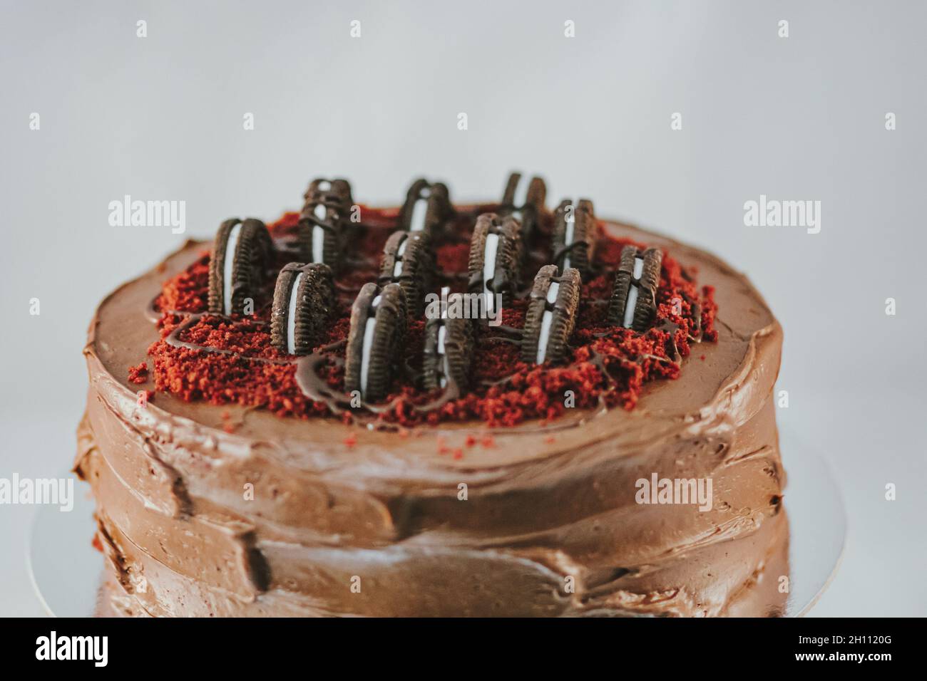 Delicious rich dark cake with Oreo on top on white background. Beautiful tasty sweet dessert with multiple layers decorated with cookies Stock Photo