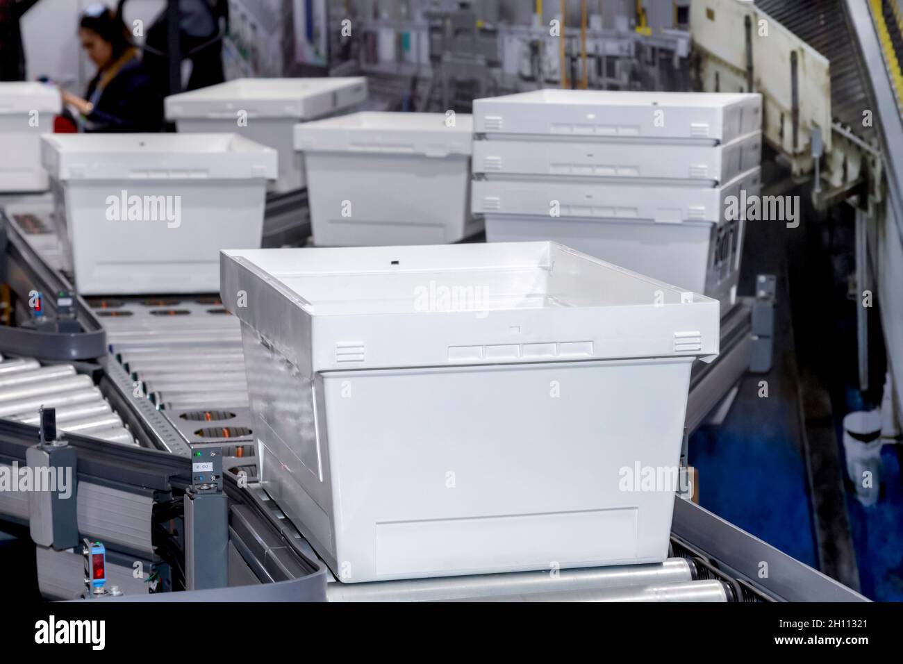 white plastic containers box on conveyor belt rollers in distribution warehouse at product manufacturing. Logistic warehouse and parcels transportation Stock Photo