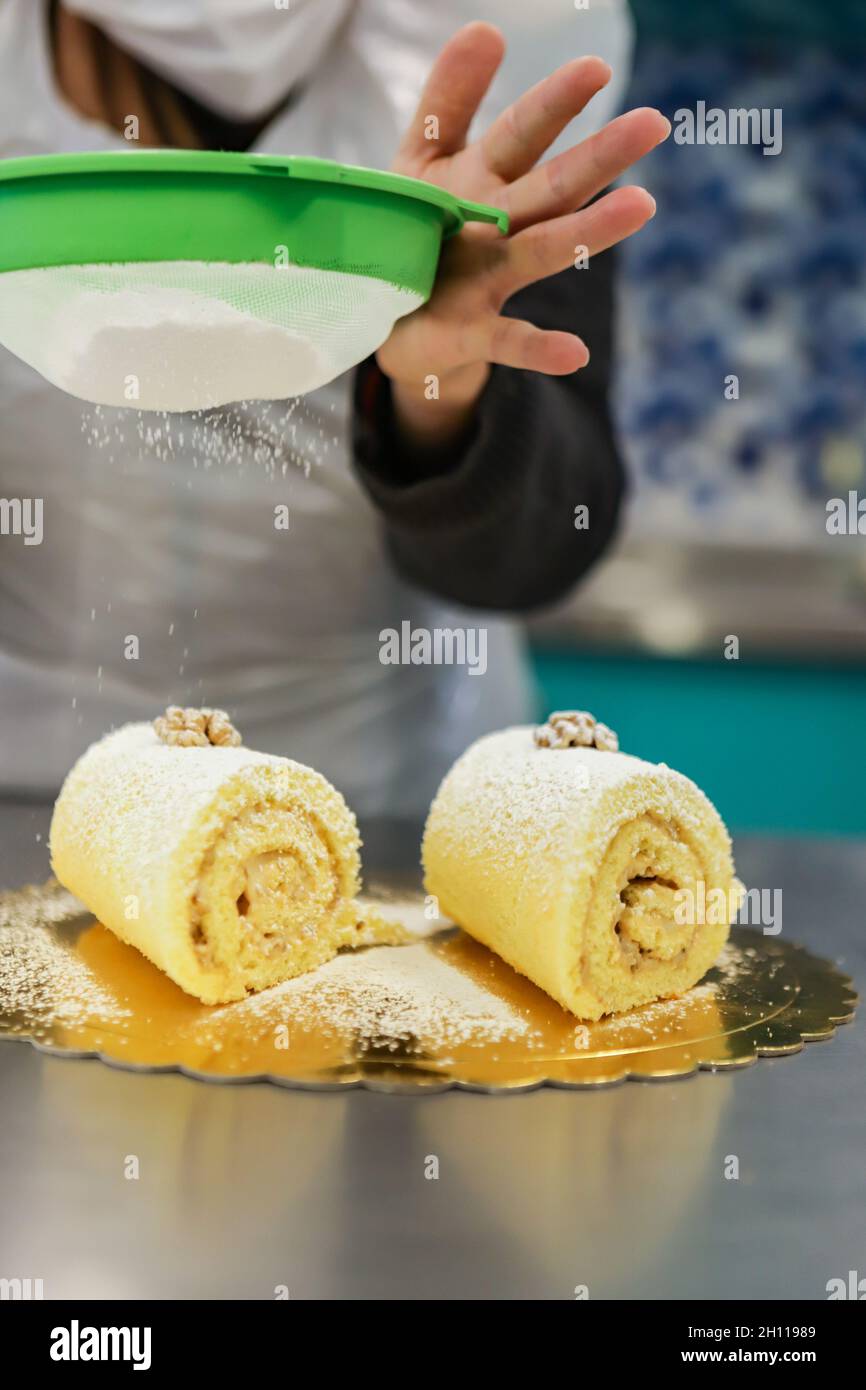 Rocambole is a sweet soft stuffed dough. In the photo, this confectioner's candy receives the sugar coating being sifted Stock Photo