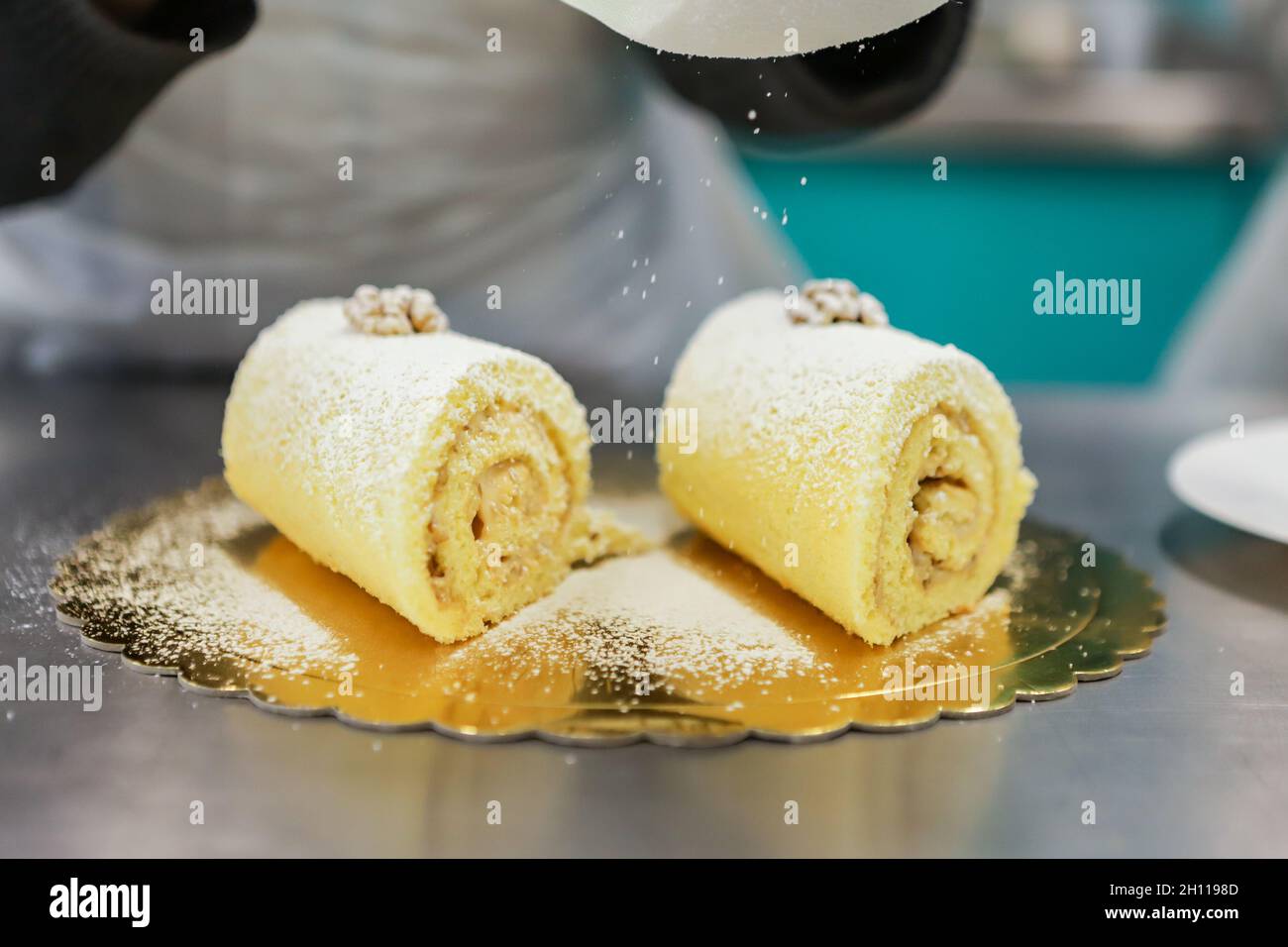 Rocambole is a sweet soft stuffed dough. In the photo, this confectioner's candy receives the sugar coating being sifted Stock Photo