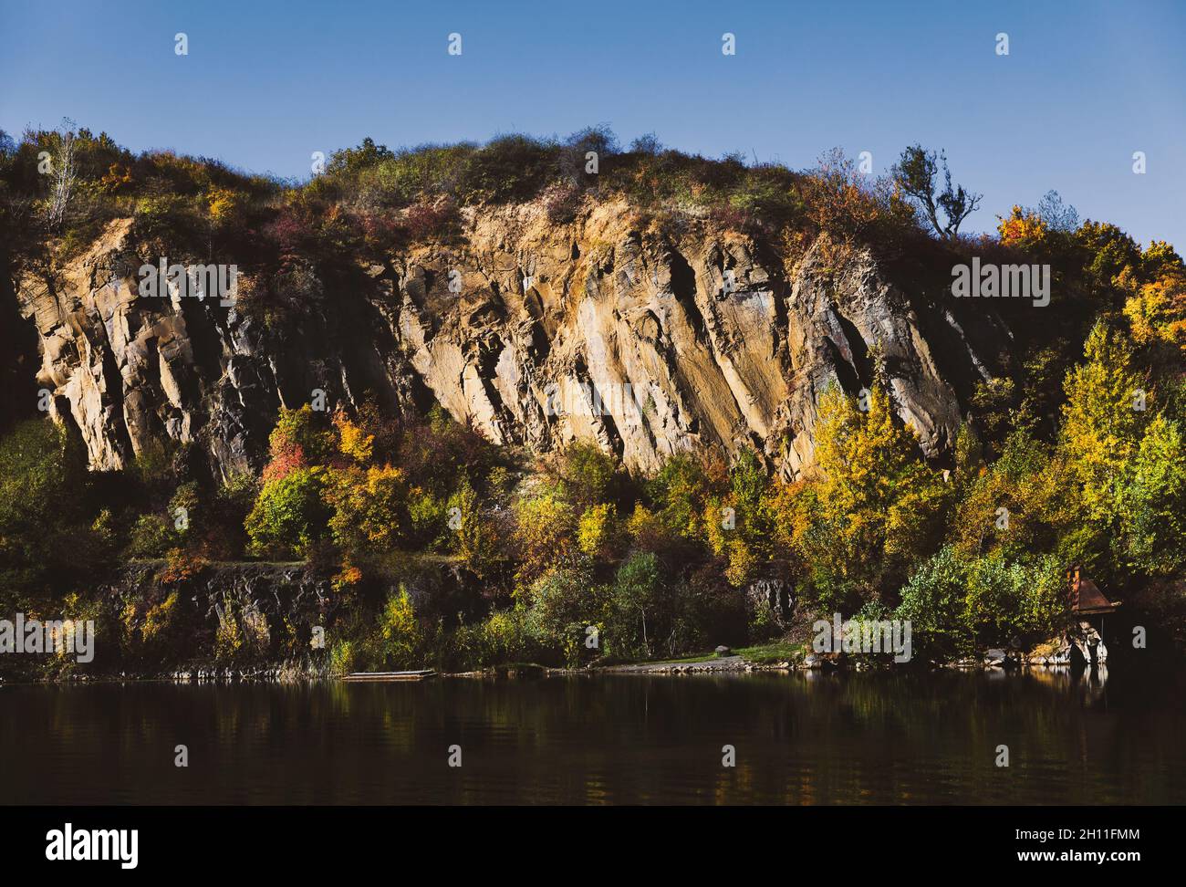 Golden autumn with colourful trees in old flooded quarry. Rocks, lake ...
