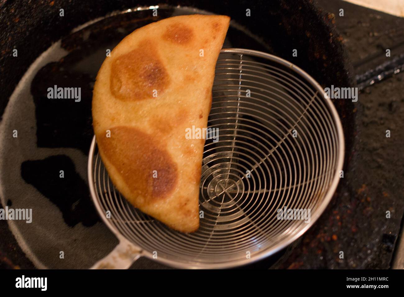 Closeup of newly cooked empanada scooped out from a pot and drained Stock Photo