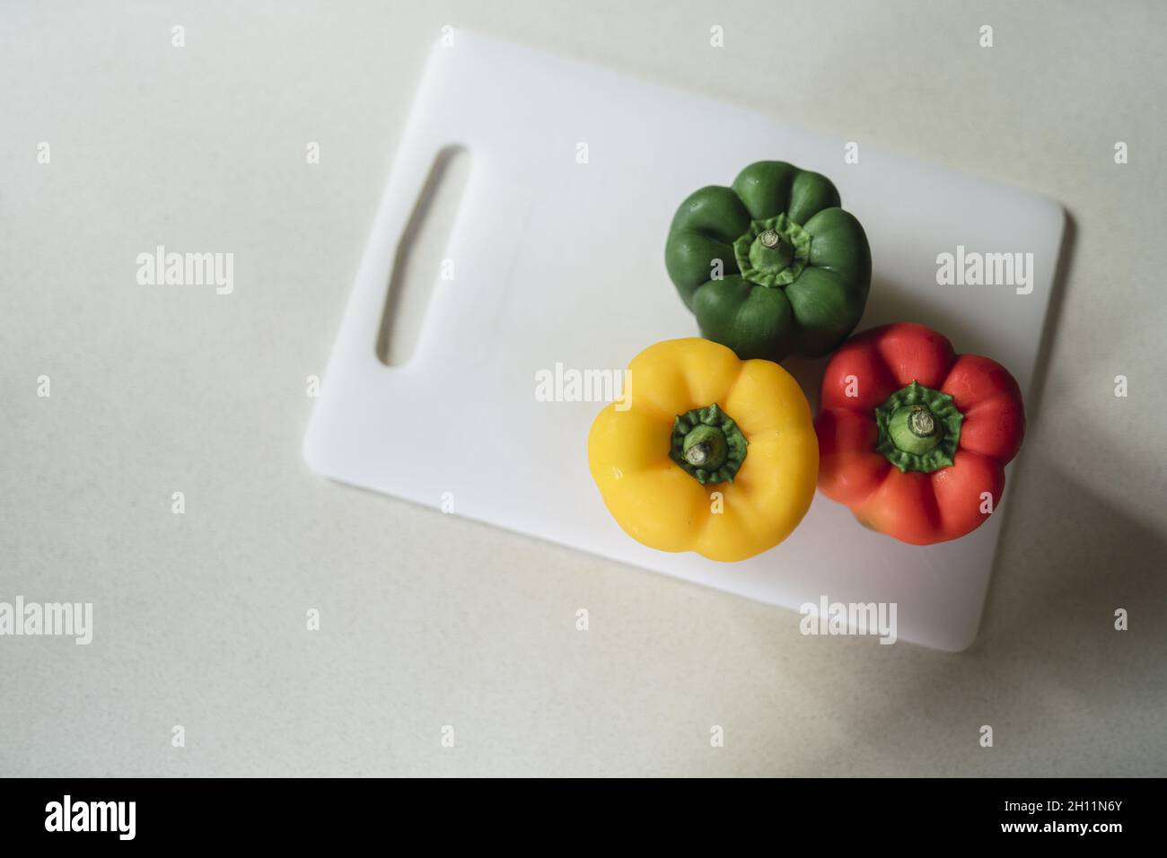 High angle shot of three different colored peppers on a plastic board Stock Photo