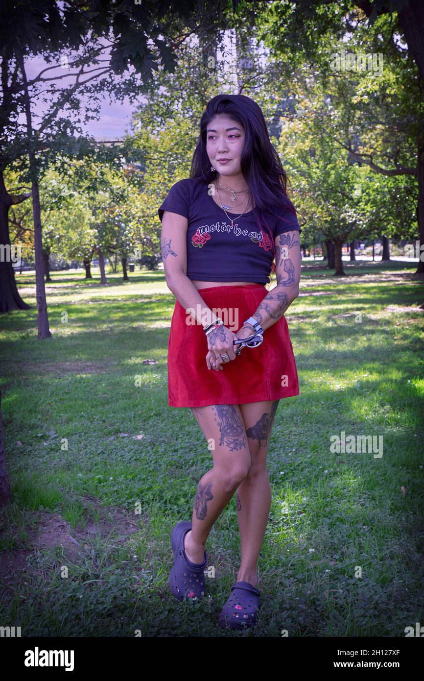 An attractive young lady with multiple tattoos and a very personal style poses for photos in a park in Queens, New York City. Stock Photo