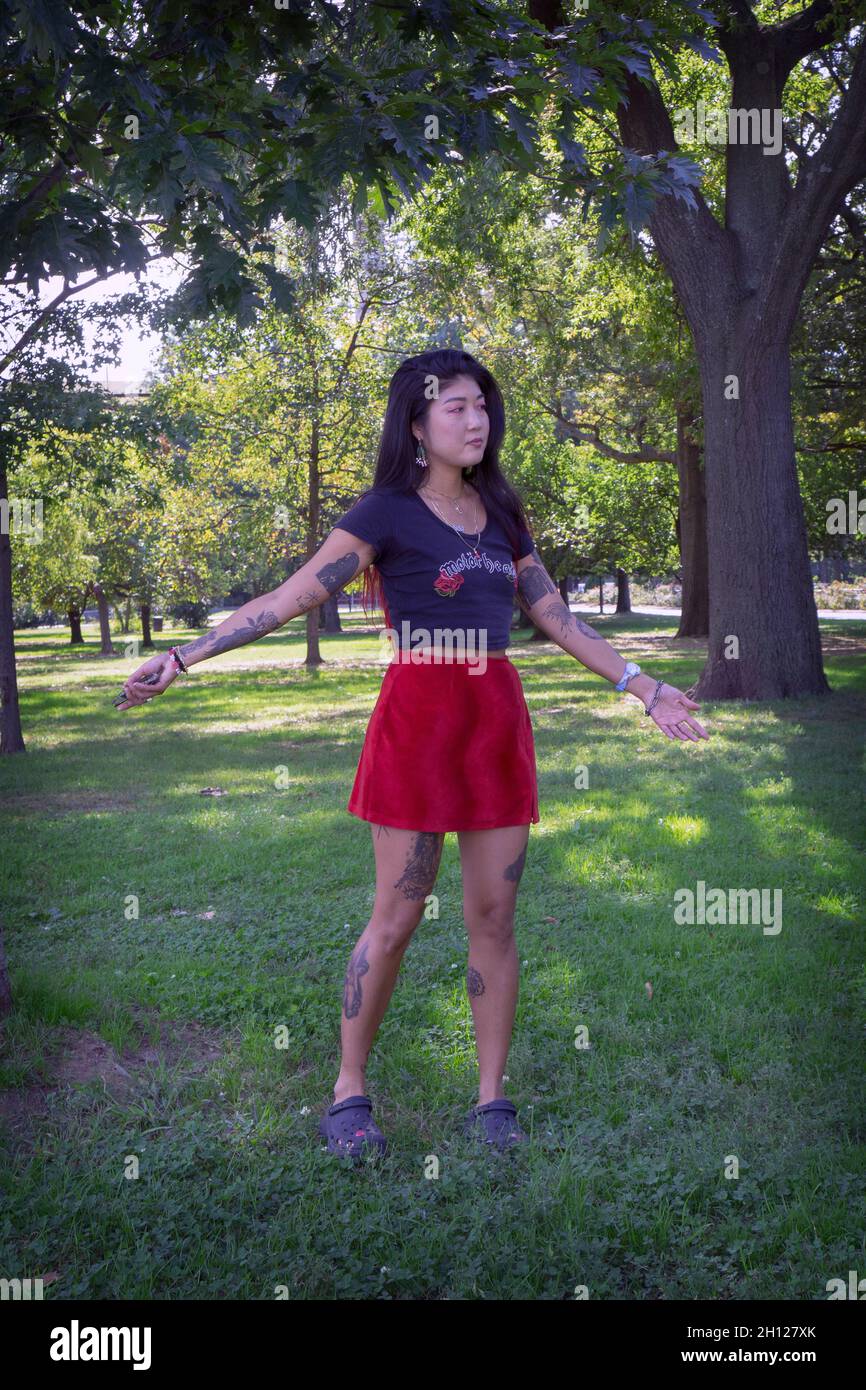 An attractive young lady with multiple tattoos and a very personal style poses for photos in a park in Queens, New York City. Stock Photo