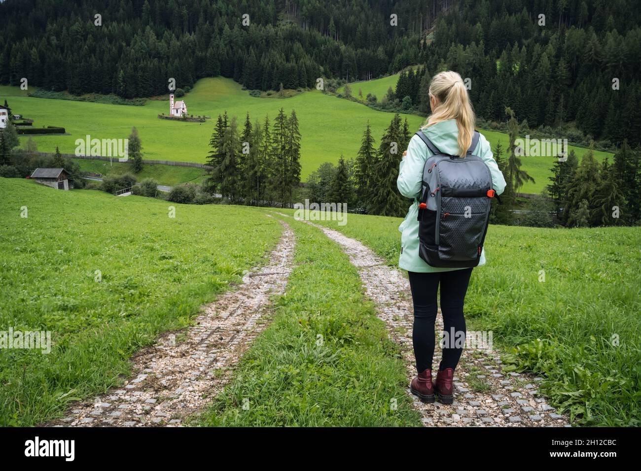 Woman with backpack on hiking trail to St. Johann church in Val di Funes valley, Dolomites, Italy, Europe Stock Photo