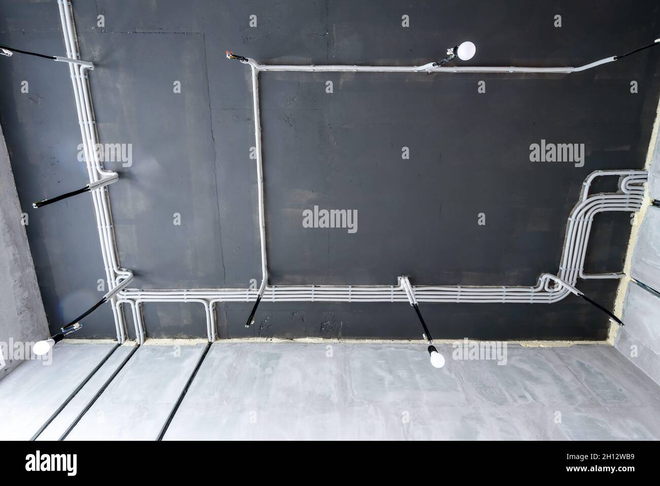 Electrical cables and pipes on house concrete ceiling. Modern plastic hoses and conduits with wires in room. Lines of pvc wiring tubes after professio Stock Photo