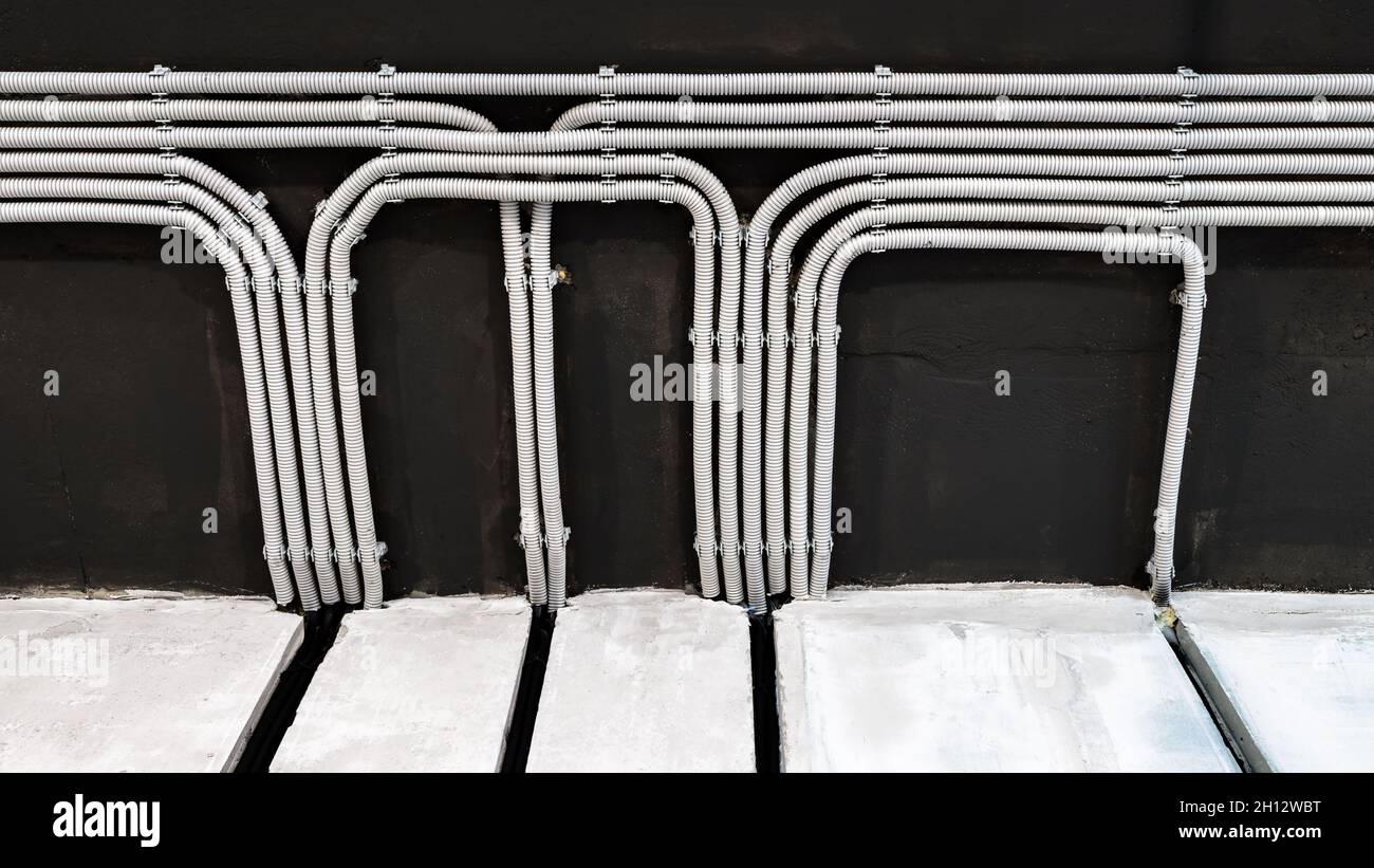 Electrical cables and pipes on house concrete ceiling. Modern plastic hoses and conduits with wires in room. Lines of pvc wiring tubes after professio Stock Photo