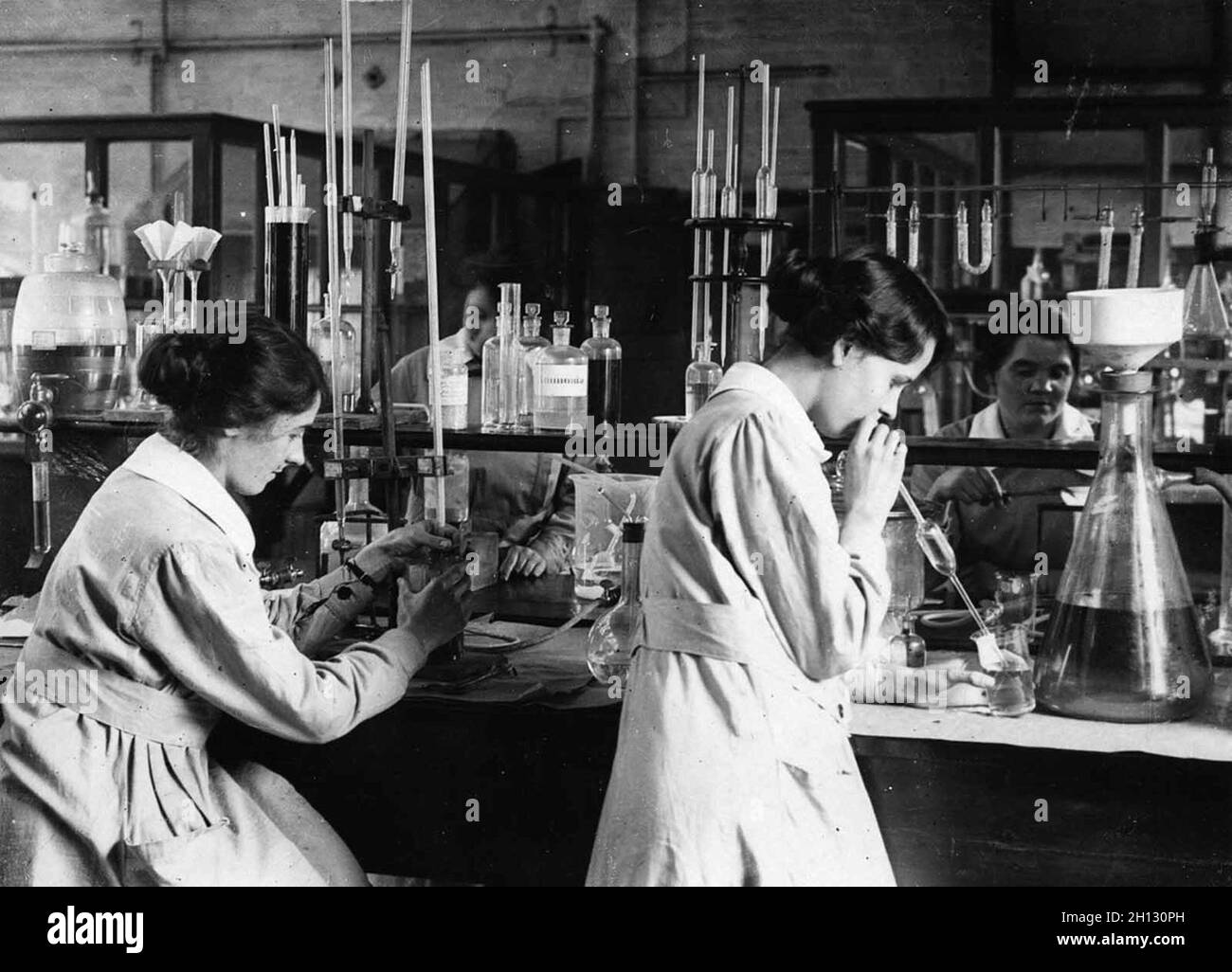 Women working in a chemical laboratory in a factory during WW1 (and the woman on the right is mouth-pipetting!) Stock Photo