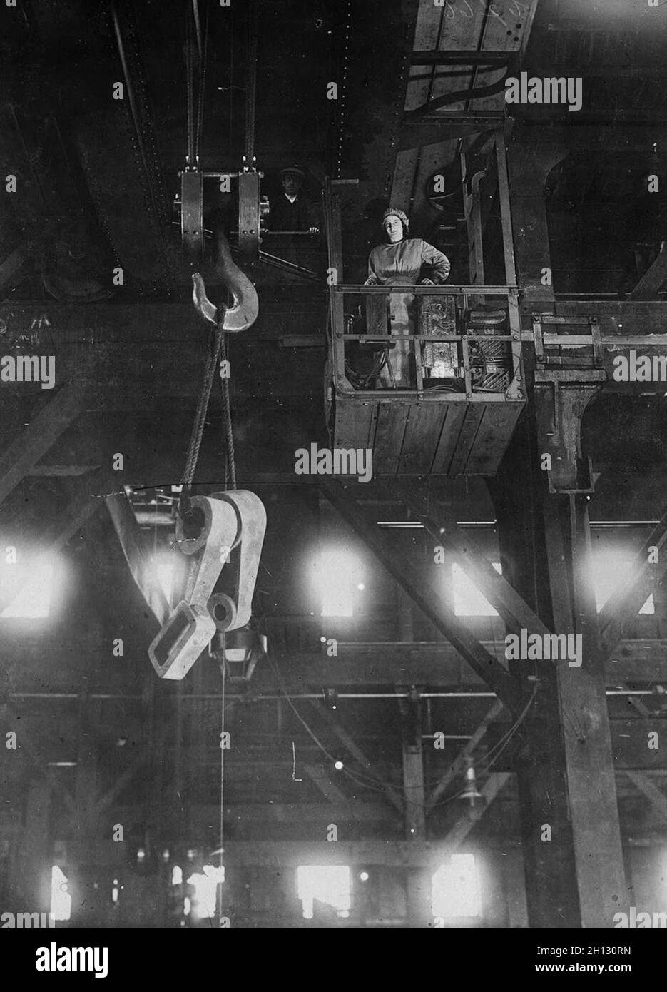 A woman operating a heavy crane in a factory during WW1. Stock Photo