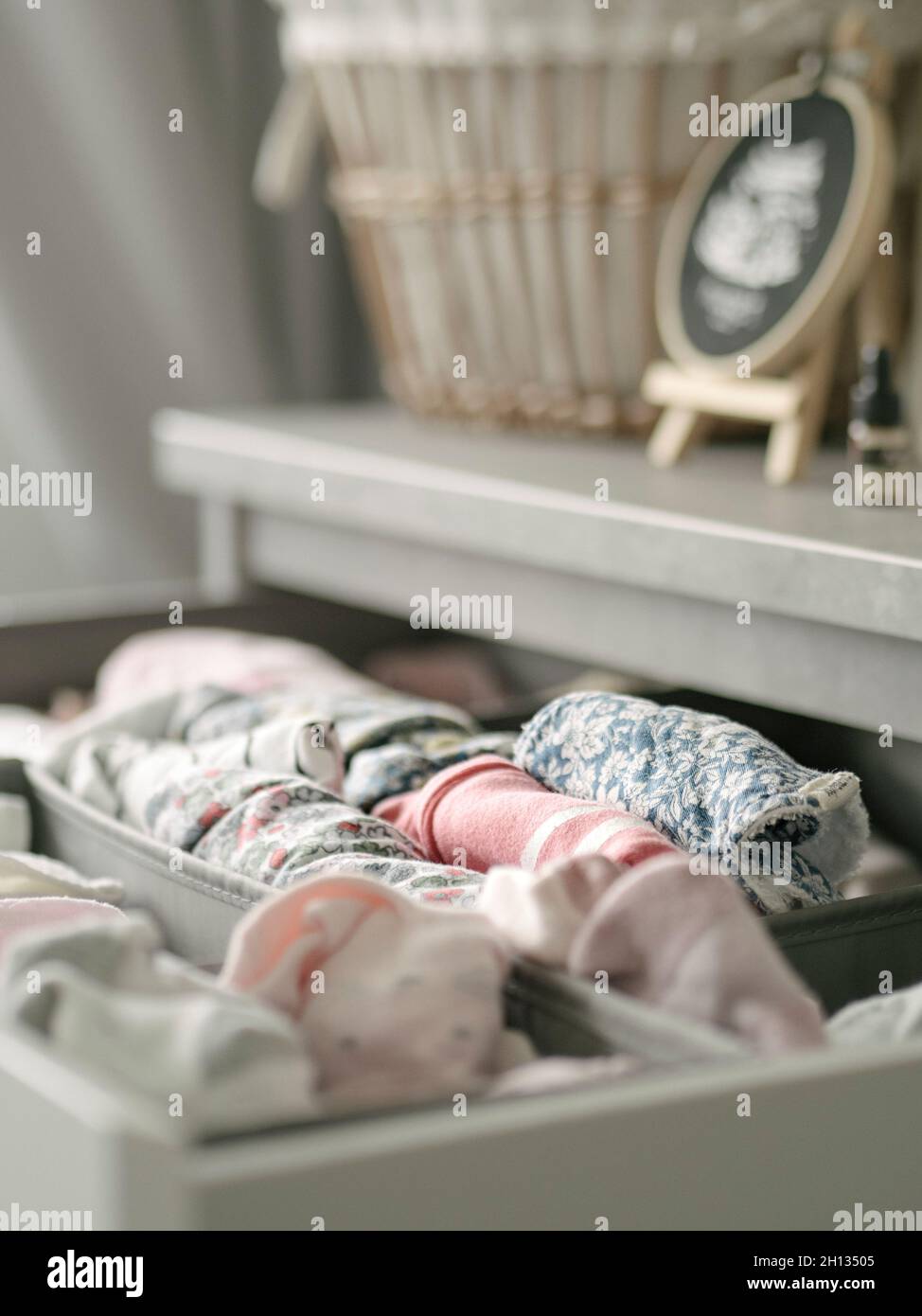 Baby clothes and bibs in a drawer with woven basket Stock Photo