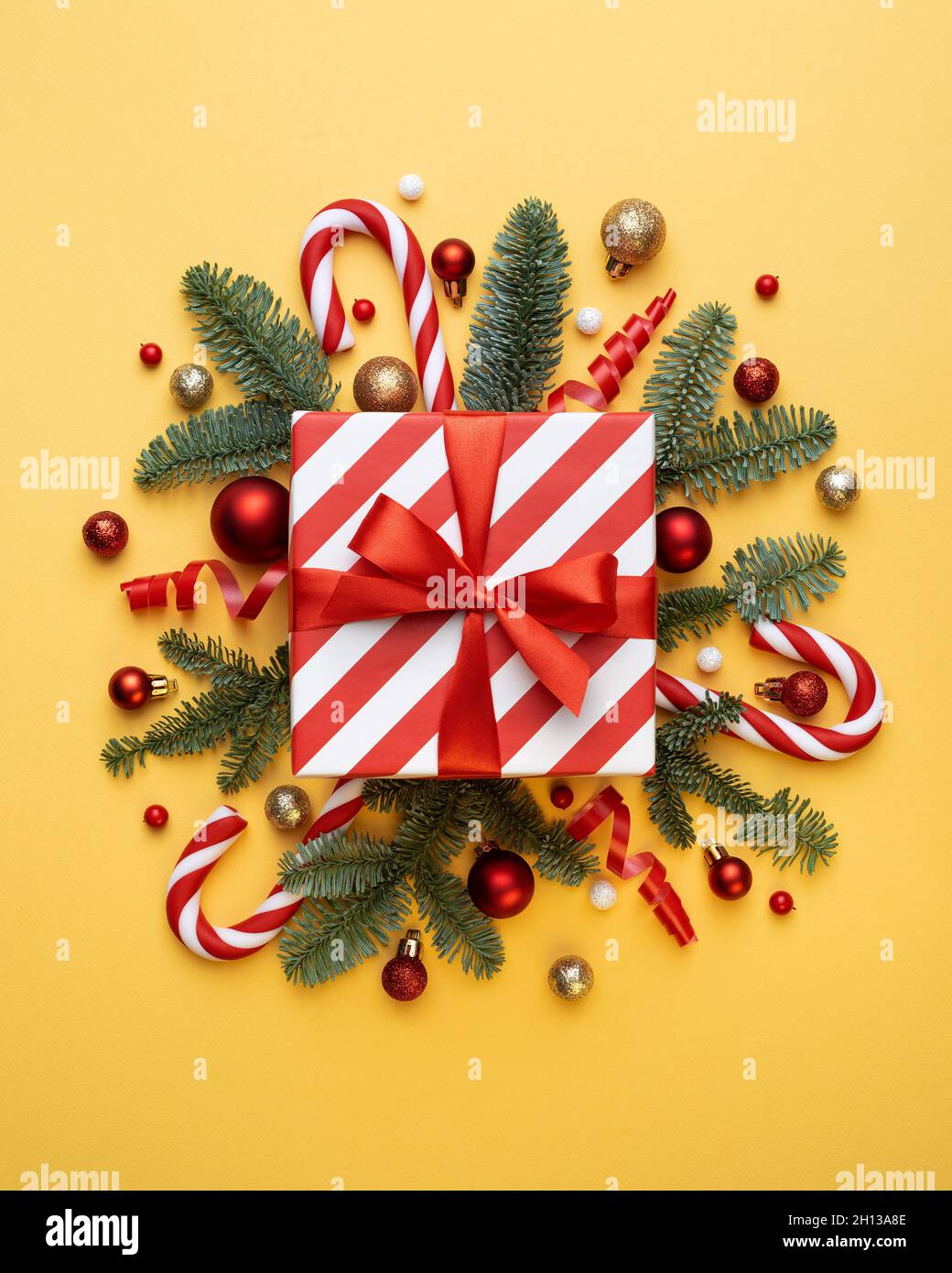 Christmas card with gift box, candy cane, Christmas balls, and fir tree branches on yellow background Stock Photo
