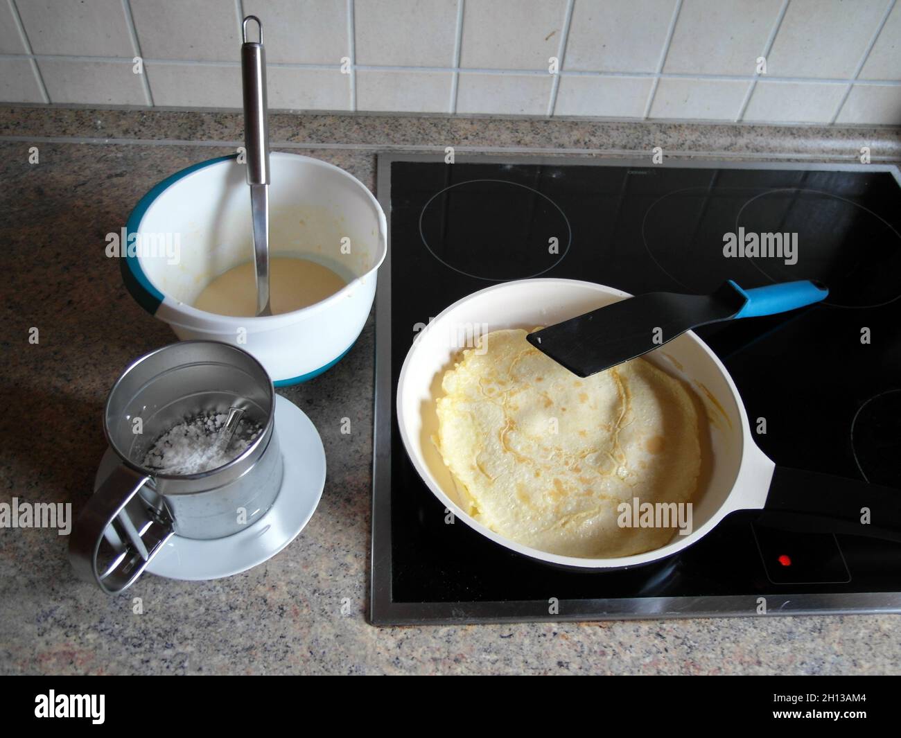 In the kitchen: bowl of batter and pan with pancakes on the stove and sugar shaker Stock Photo