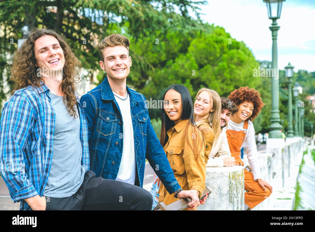 Portrait of happy college friends smiling and greeting looking in camera - Beautiful cheerful multiethnic friends in the city - Friendship concept Stock Photo
