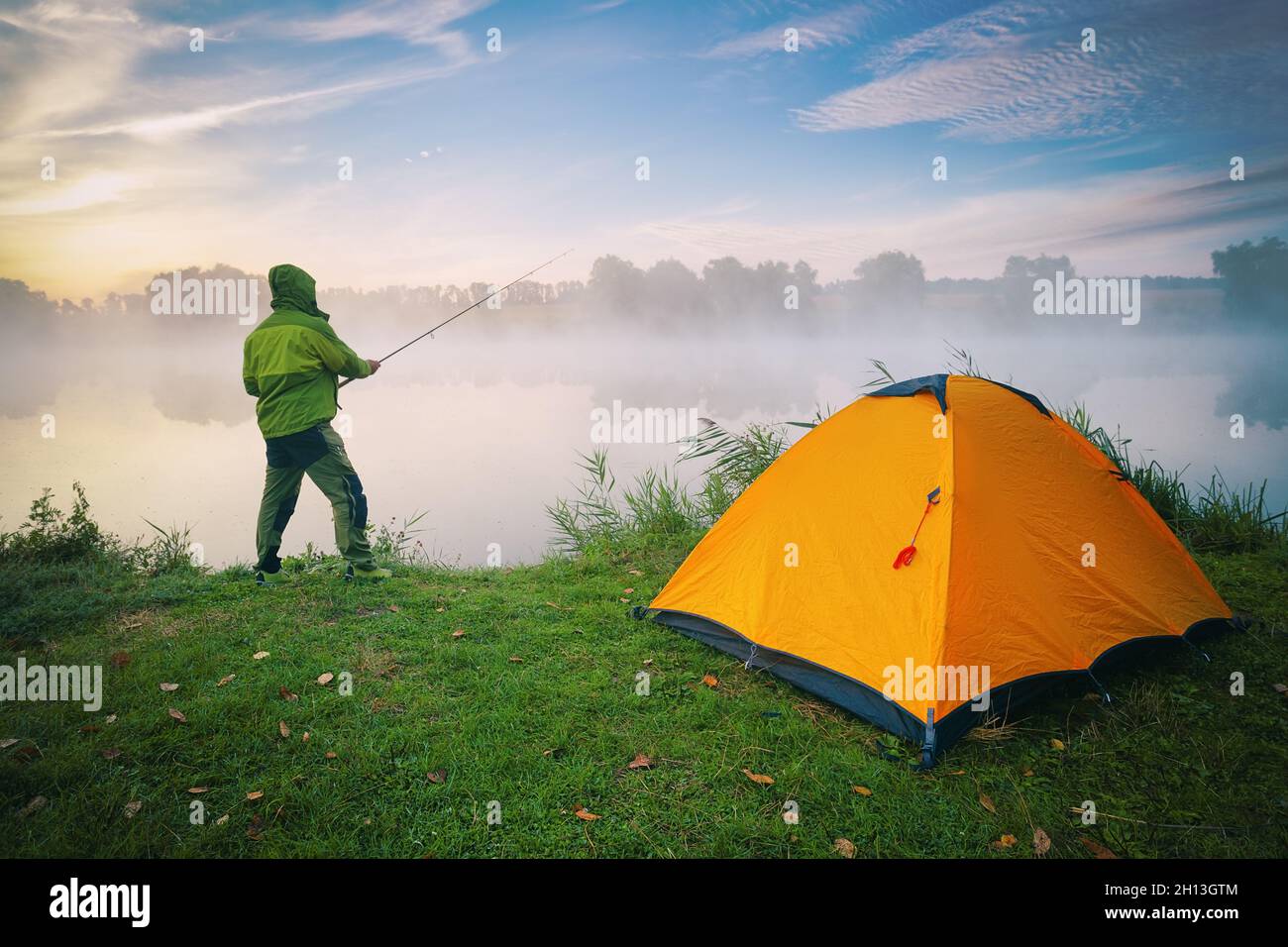 Fisherman by lake with orange tent on foggy morning Stock Photo