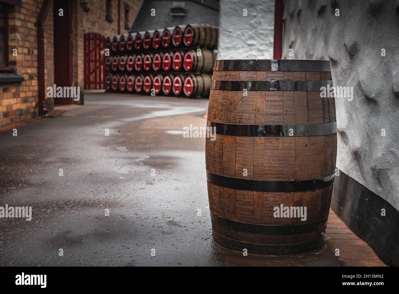 Old, vintage wooden whiskey barrel in an alley with rows of barrels in