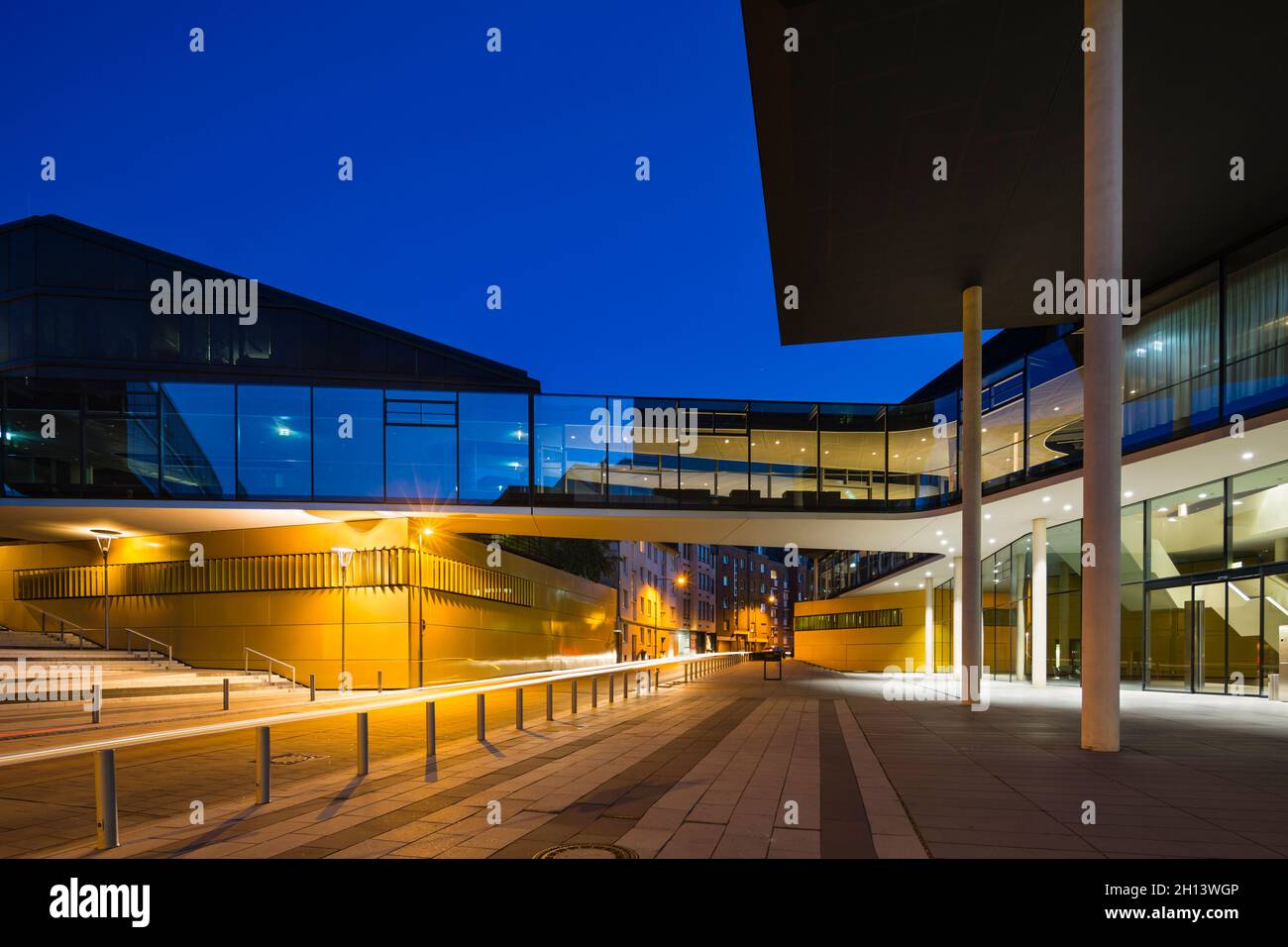 Modern architecture with a glass bridge crossing a street in the center of Aachen, Germany with night blue sky. Taken with a shift lens for straight p Stock Photo