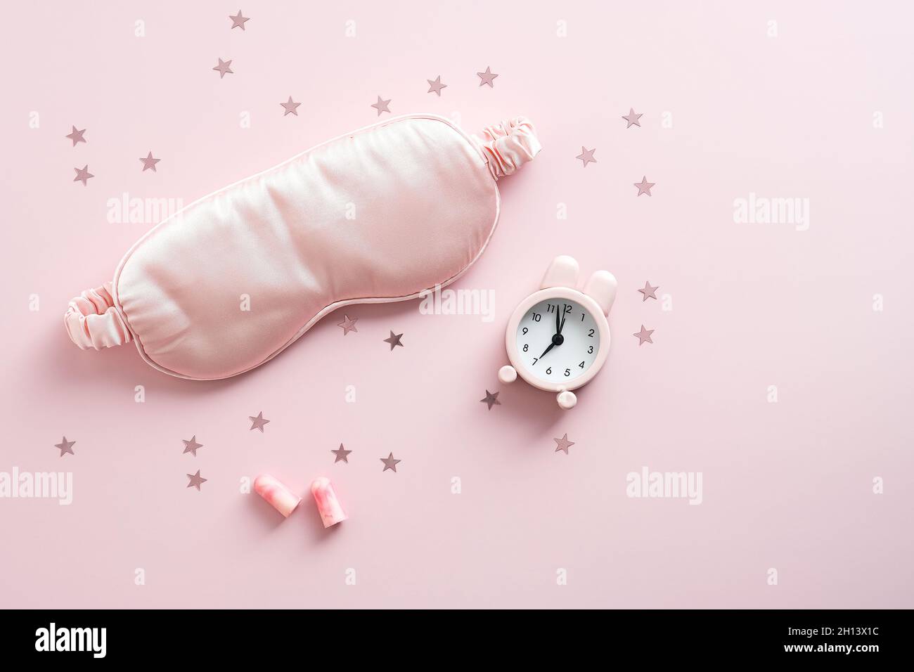 Sleep mask, earplugs, alarm clock on pastel pink background. Treatments