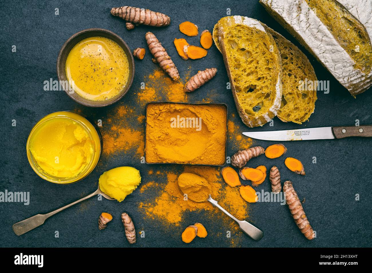 Turmeric powder, root, ghee, bread and golden milk on a slate background Stock Photo