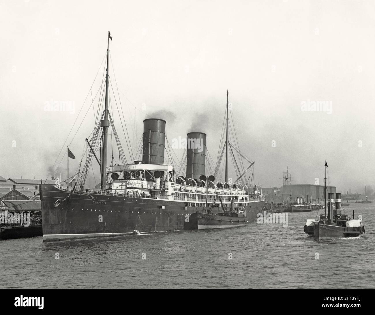 RMS Campania in port in the early 1900s – the ship was a British ocean liner owned by the Cunard Steamship Line Shipping Co, built in Govan, Scotland. Launched in1892, she was the largest and fastest passenger liner when she entered service in 1893, winning the prestigious Blue Riband. Her last passenger voyage was in 1914. Campania had a reprieve from being scrapped. The UK Admiralty converted her to an armed merchant cruiser that could carry seaplanes. HMS Campania looked little like her original configuration. She served until 1918 when she sank in the Firth of Forth – a vintage 1900s photo Stock Photo