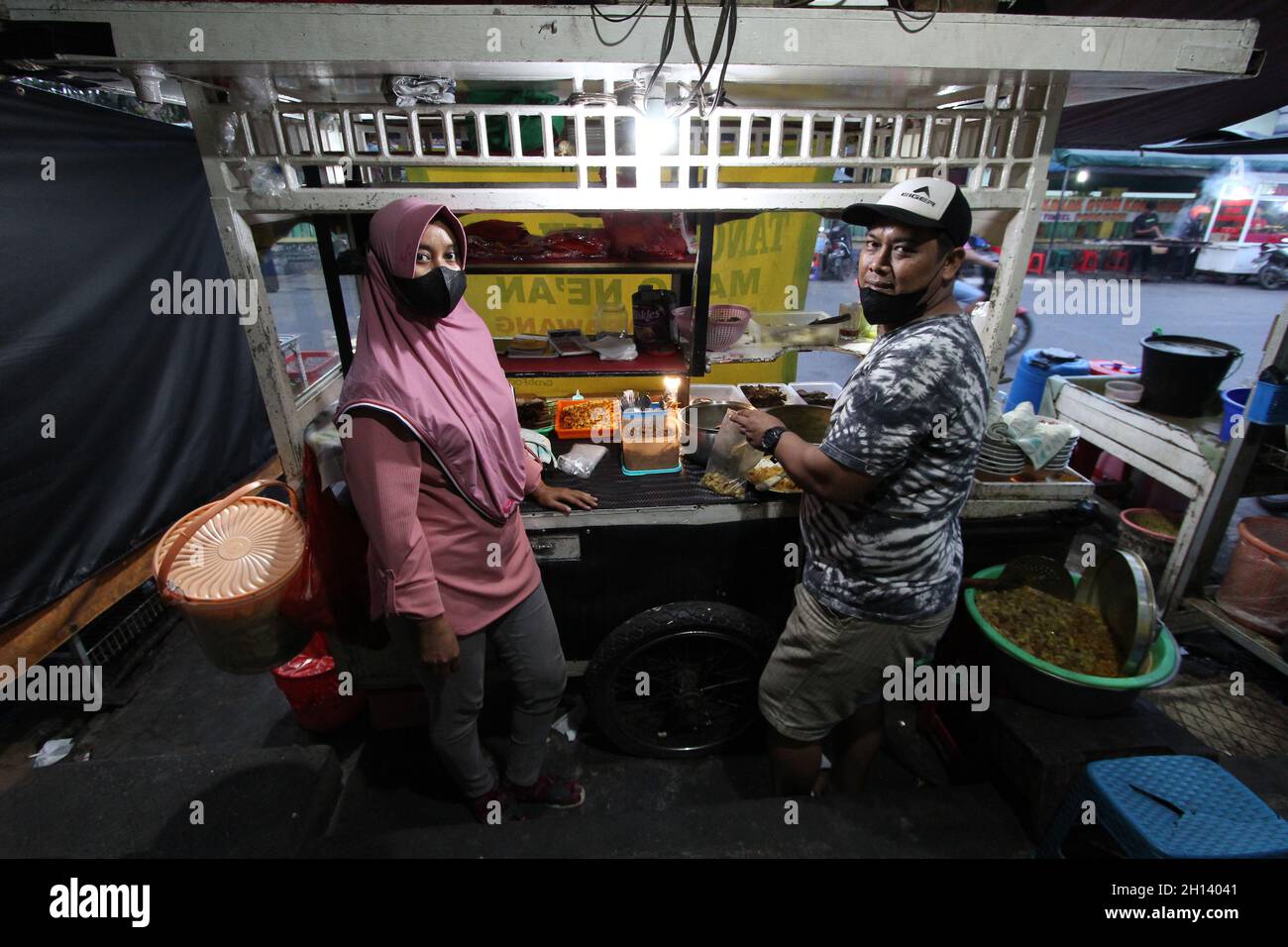 Karawang, Indonesia. 15th Oct, 2021. Endi, 39, the son-in-law of the shop owner and his wife Devi, 32, the daughter of one of the owners of the Soto Tangkar stall, Mang Nean, who has been selling since 1980, poses for a photo at the legendary food stall Soto Tangkar typical of Karawang on Jalan Dewi Sartika, West Karawang, Karawang, West Java, Indonesia. This soto dish uses beef ribs and beef leg veins seasoned with turmeric and chili. It tastes savory and slightly sweet. Interestingly, this delicious dish is cooked traditionally. Almost all ingredients are steamed in a pot over coals of firew Stock Photo