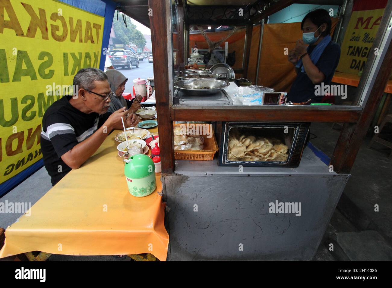 Karawang, Indonesia. 15th Oct, 2021. Consumers enjoy food at the Soto Tangkar Mang Endi stall, one of the legendary foods typical of Karawang on Jalan Dewi Sartika, West Karawang, Karawang, West Java, Indonesia. This soto dish uses beef ribs and beef leg veins seasoned with turmeric and chili. It tastes savory and slightly sweet. Interestingly, this delicious dish is cooked traditionally. Almost all ingredients are steamed in a pot over coals of firewood. The growth of micro, small and medium enterprises (MSMEs) economic actors in Indonesia has begun to stir in the midst of the Covid-19 pandem Stock Photo