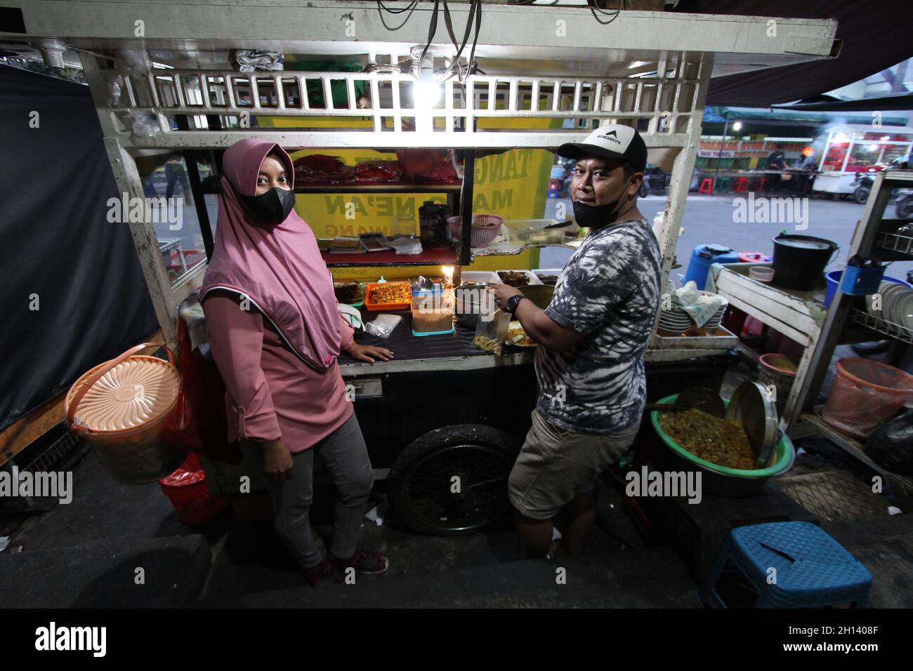Karawang, Indonesia. 15th Oct, 2021. Endi, 39, the son-in-law of the shop owner and his wife Devi, 32, the daughter of one of the owners of the Soto Tangkar stall, Mang Nean, who has been selling since 1980, poses for a photo at the legendary food stall Soto Tangkar typical of Karawang on Jalan Dewi Sartika, West Karawang, Karawang, West Java, Indonesia. This soto dish uses beef ribs and beef leg veins seasoned with turmeric and chili. It tastes savory and slightly sweet. Interestingly, this delicious dish is cooked traditionally. Almost all ingredients are steamed in a pot over coals of firew Stock Photo