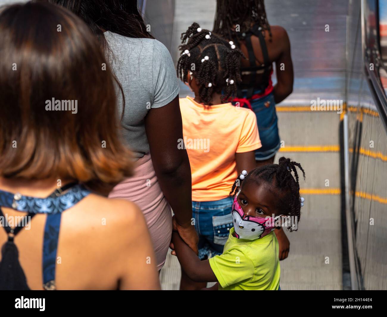 Medellin, Antioquia, Colombia - December 23 2020: Black Girl with Crossed Eyes Going Down the Electric Stairs with her Mom and her Sisters Stock Photo