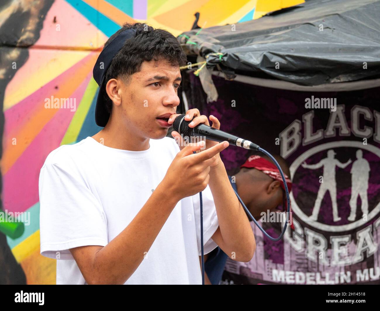 Medellin, Antioquia, Colombia - January 6 2021: Young Latin Man with Curly Hairs Sings Hip-Hop with Black Microphone against Colorful Wall Stock Photo