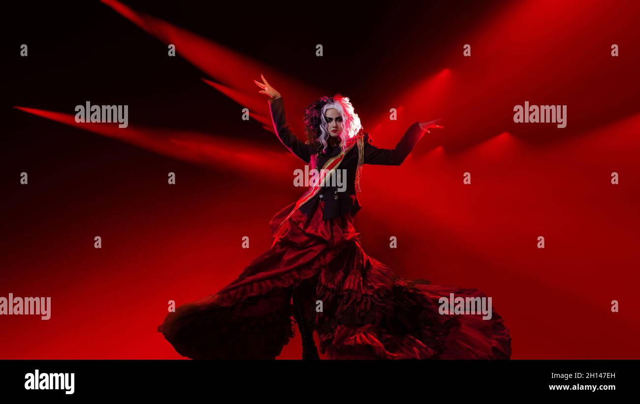 Make a performance. A bright and shocking woman on the stage in the light of red spotlights, with a black and white hairstyle is dressed in a decorate Stock Photo