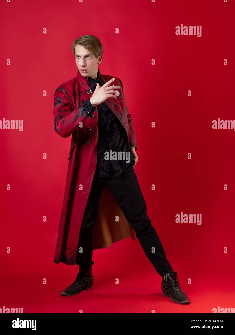 An outrageous young man in a daring red coat in a vintage noir style, photo on a red background Stock Photo