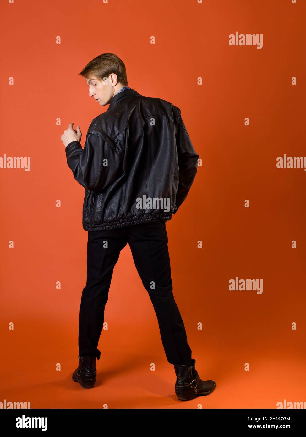 a guy in a casual plaid shirt and a leather jacket, studio photo on an orange background Stock Photo