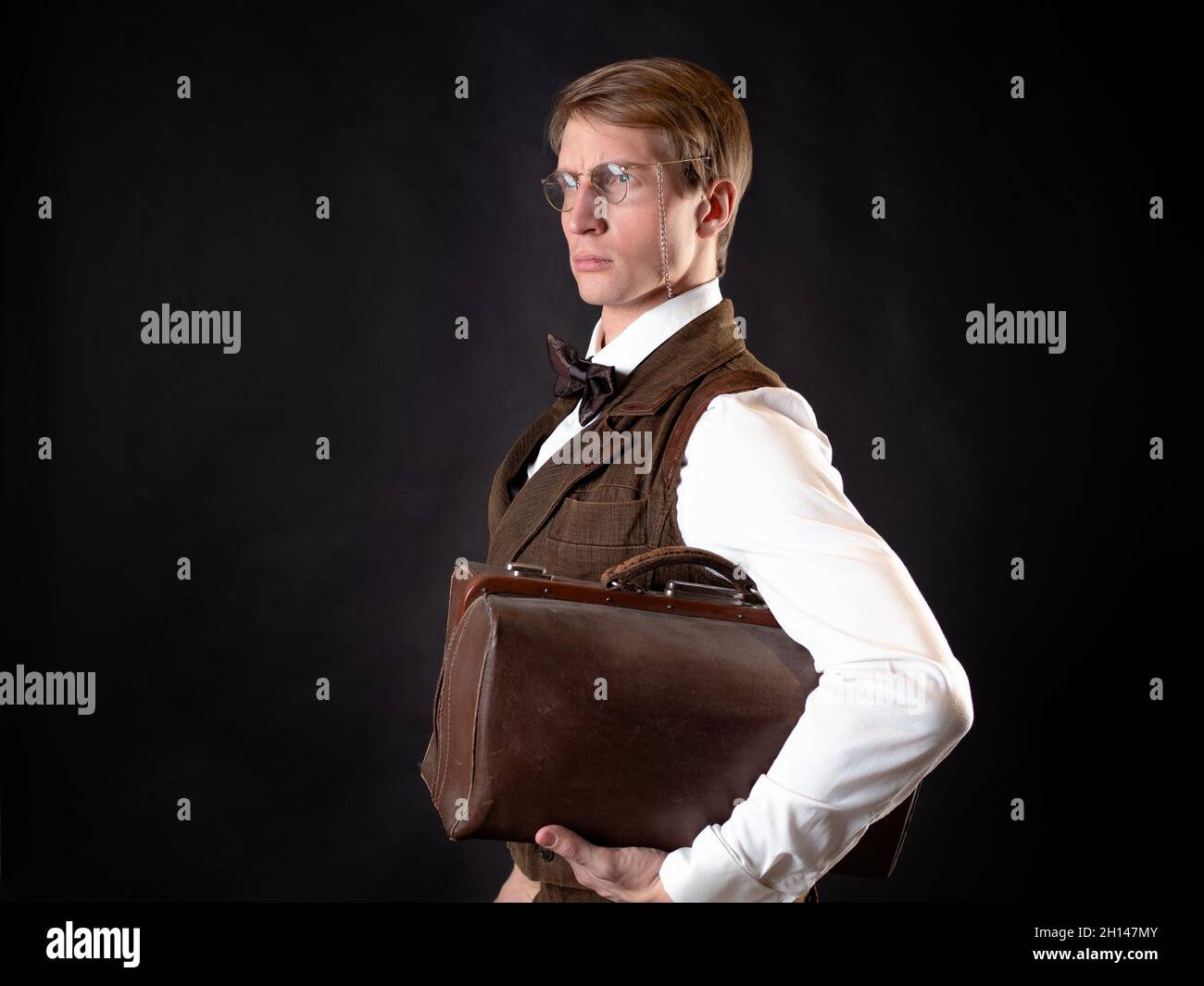 An intelligent gentleman in the Victorian style. Vintage retro suit, young attractive man in a vest and bow tie he holds his bag in his hands Stock Photo