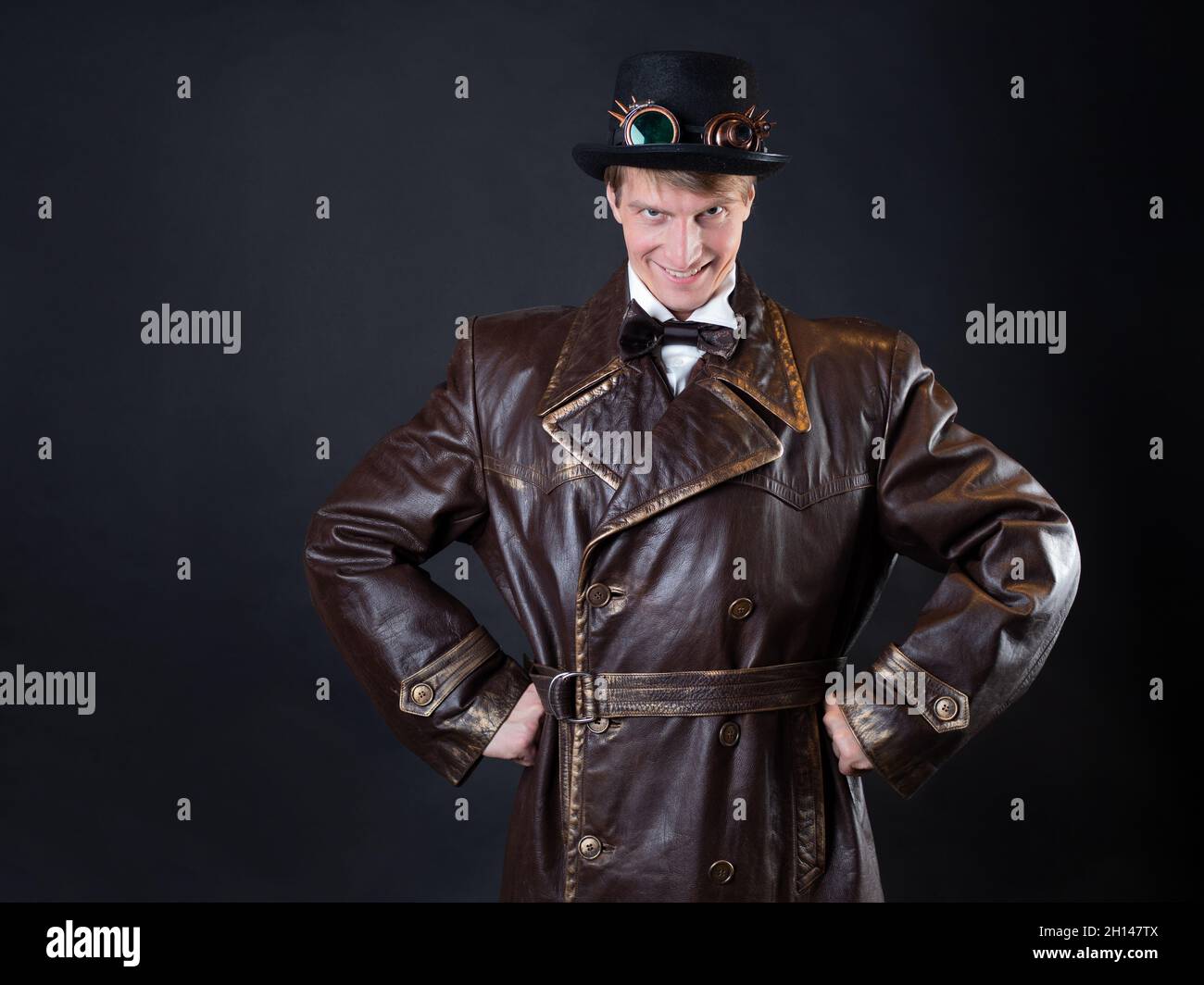 Funny man in a ridiculous leather coat and a top hat, vintage style of clothing, photo on a black background, a joking character makes stupid faces Stock Photo