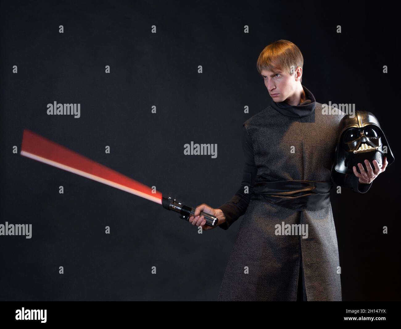 A villain with a red lightsaber, a young man in a long robe does fighting poses, fantasy or science fiction Stock Photo