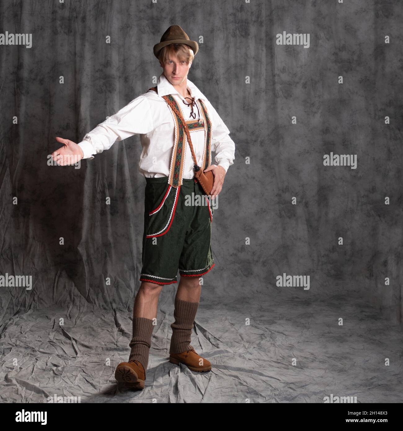 A young man in a national Bavarian suit with shorts on suspenders and a hat. Charismatic Bavarian full-length portrait, pose with outstretched arms, p Stock Photo