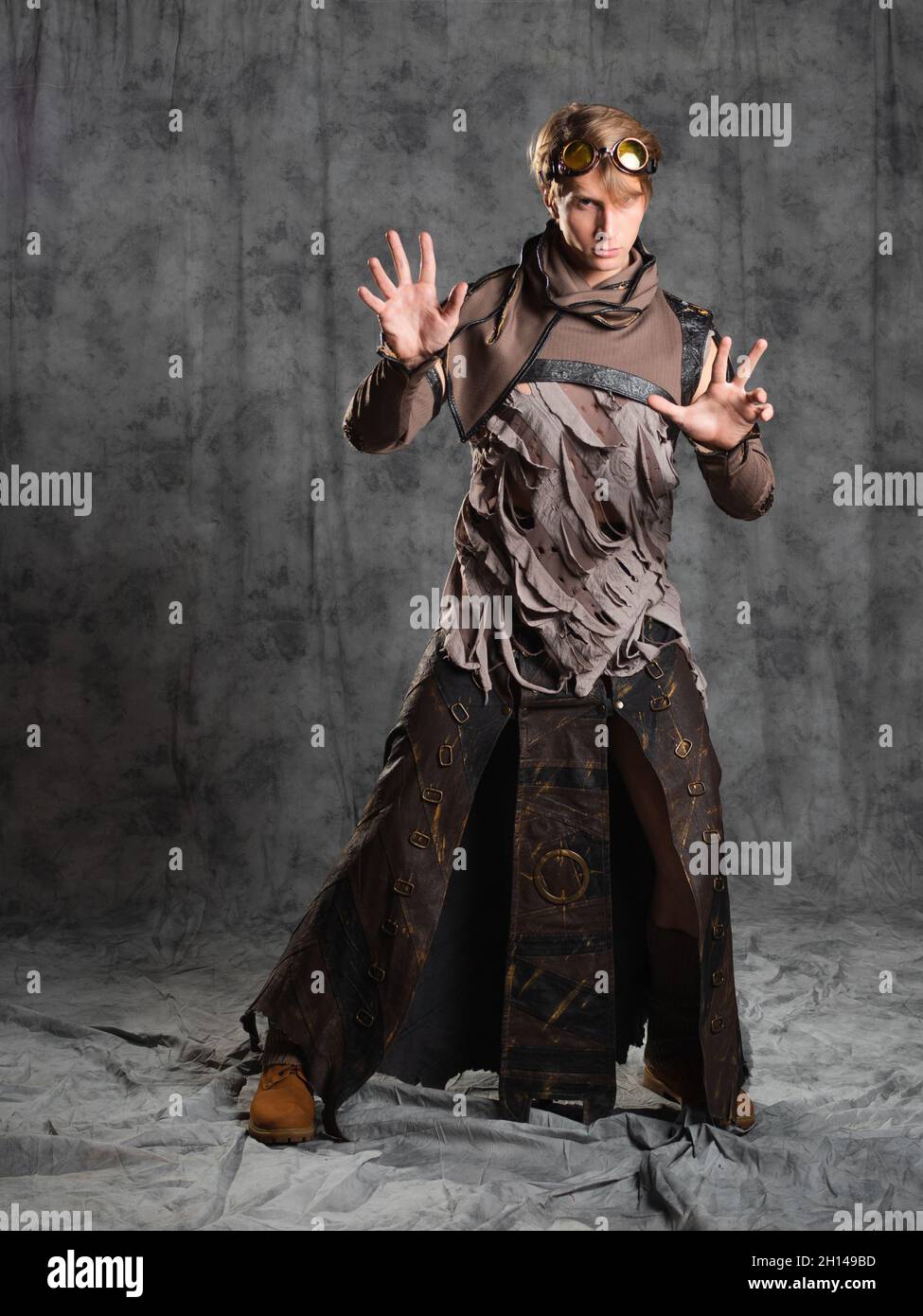 Steampunk or post-apocalyptic style character, a young man in a grunge suit. A jacket with fastened sleeves decorated with slits and a long leather sk Stock Photo