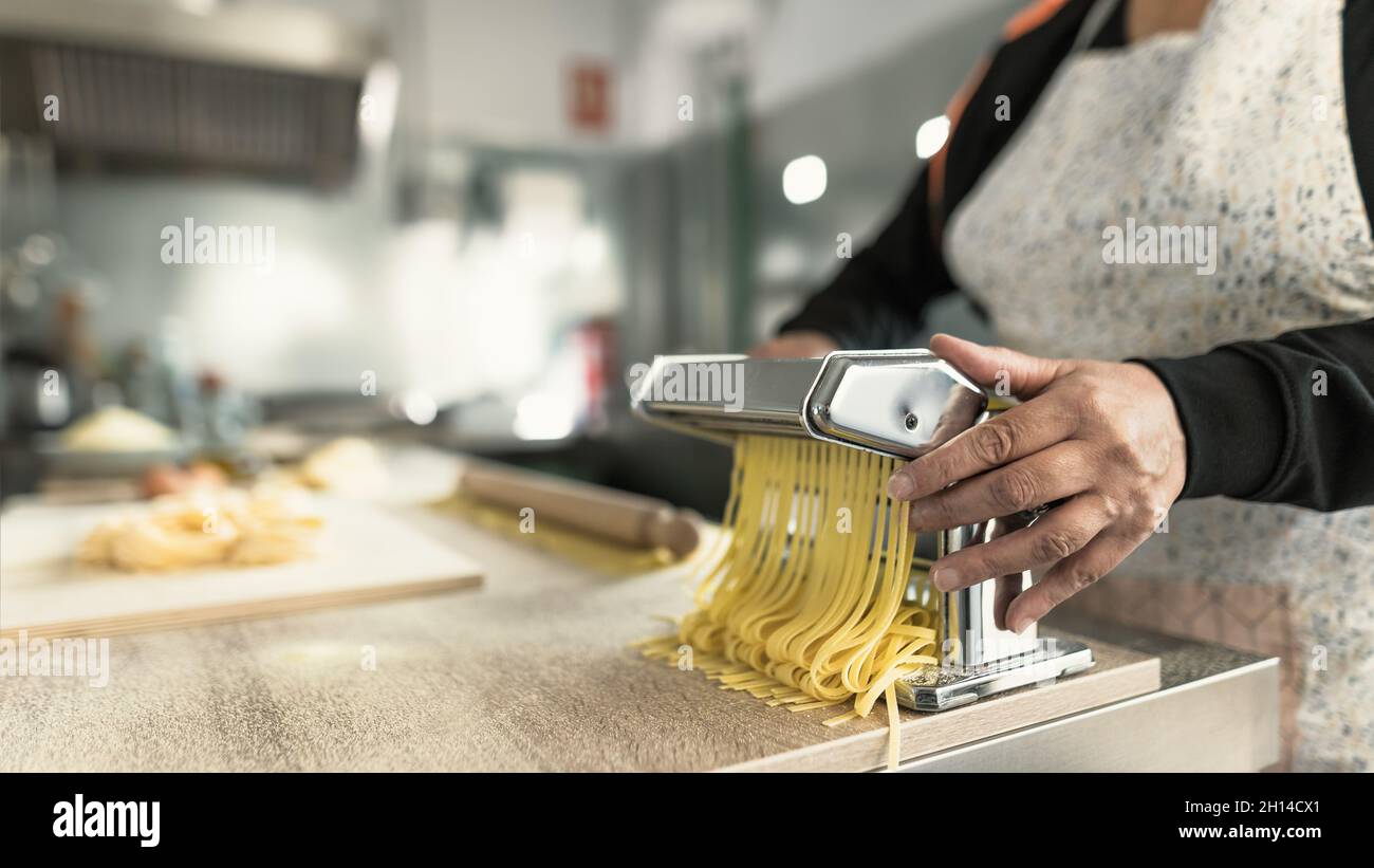 Close up female hands preparing fresh fettucine pasta using traditional machine Stock Photo