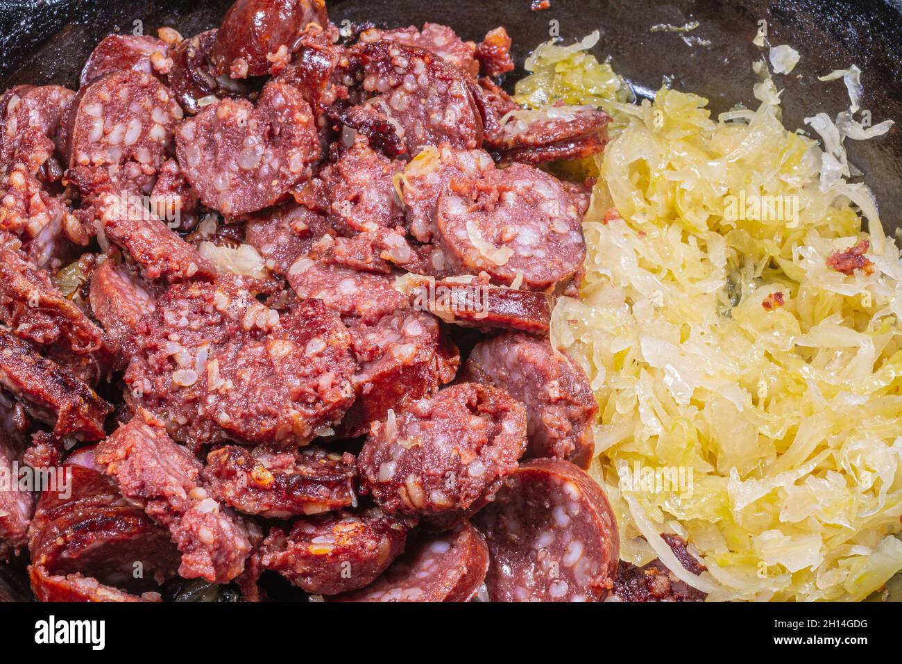 Fried Sausage slices with barley grains and Sauerkraut on cast iron frying pan Stock Photo